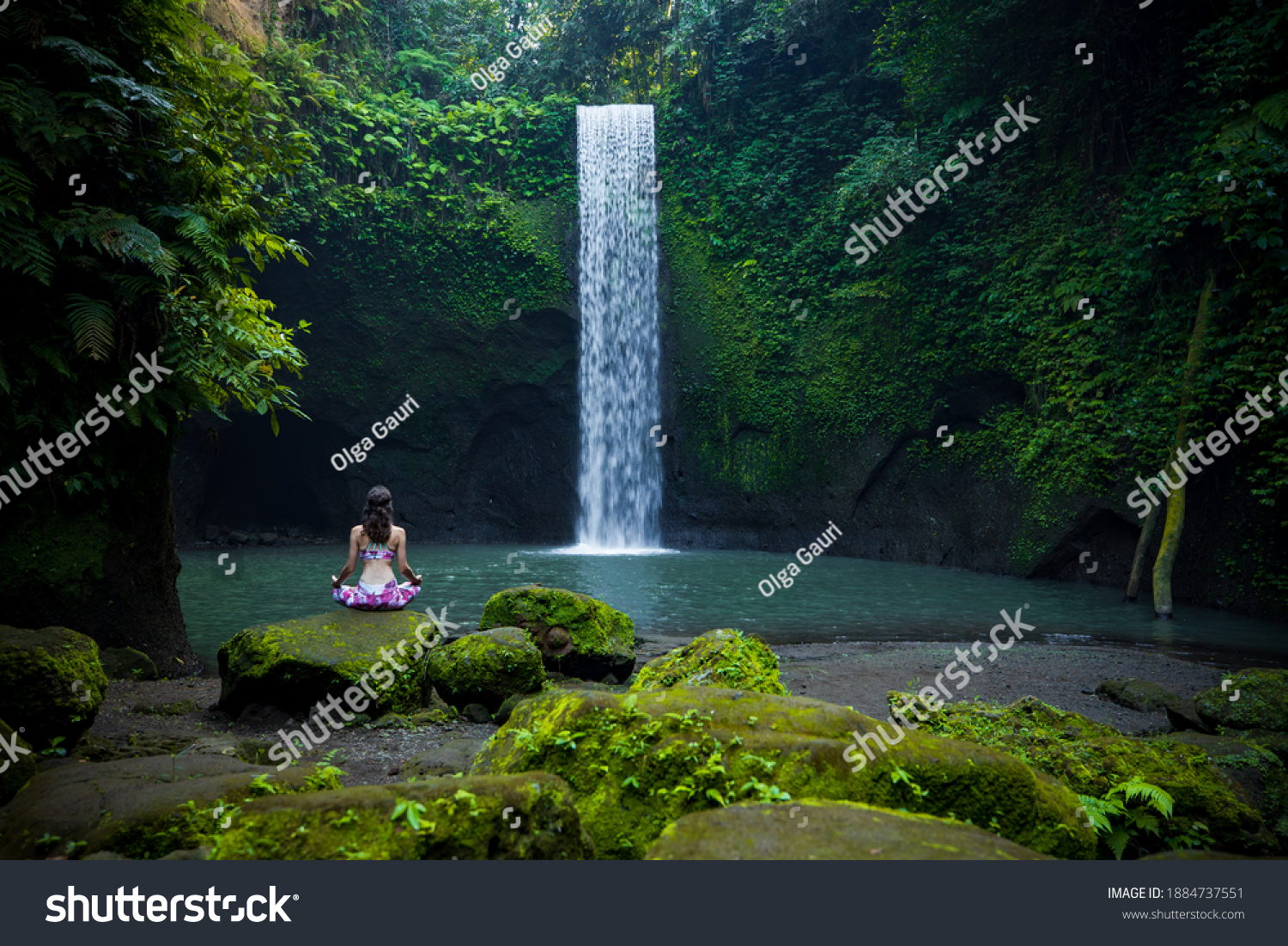 Yoga lotus pose. Young Caucasian woman sitting on the stone, meditating, practicing yoga, pranayama at waterfall. Hands in gyan mudra. Yoga retreat. View from back. Tibumana waterfall, Bali, Indonesia #1884737551