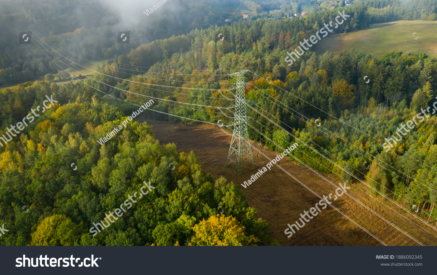 Aerial view of the high voltage power lines and high voltage electric transmission on the terrain surrounded by trees at sunlight #1886092345
