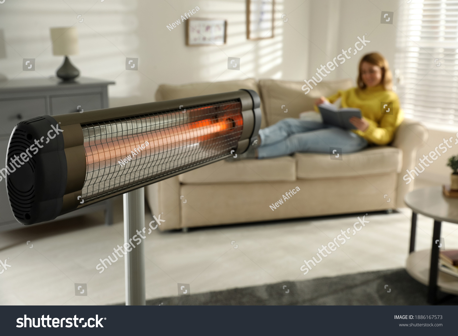 Woman reading book in living room, focus on electric infrared heater #1886167573