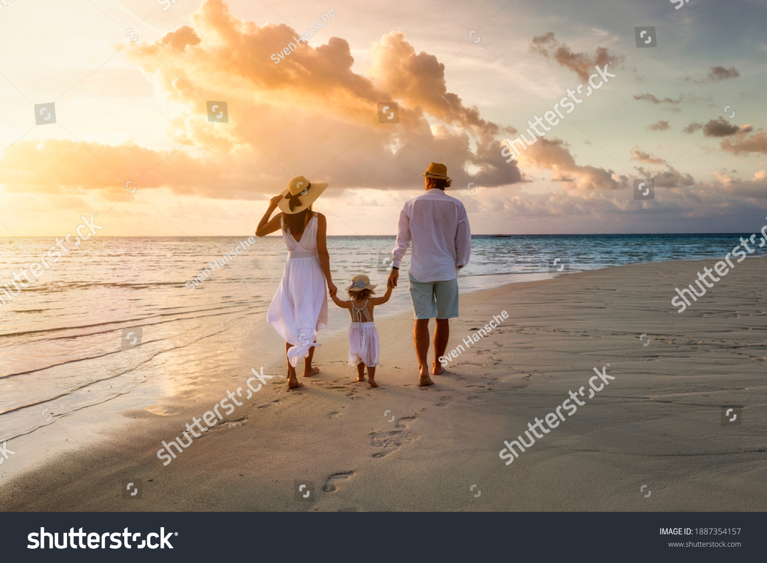 A elegant family in white summer clothing walks hand in hand down a tropical paradise beach during sunset tme and enjoys their vacation time #1887354157