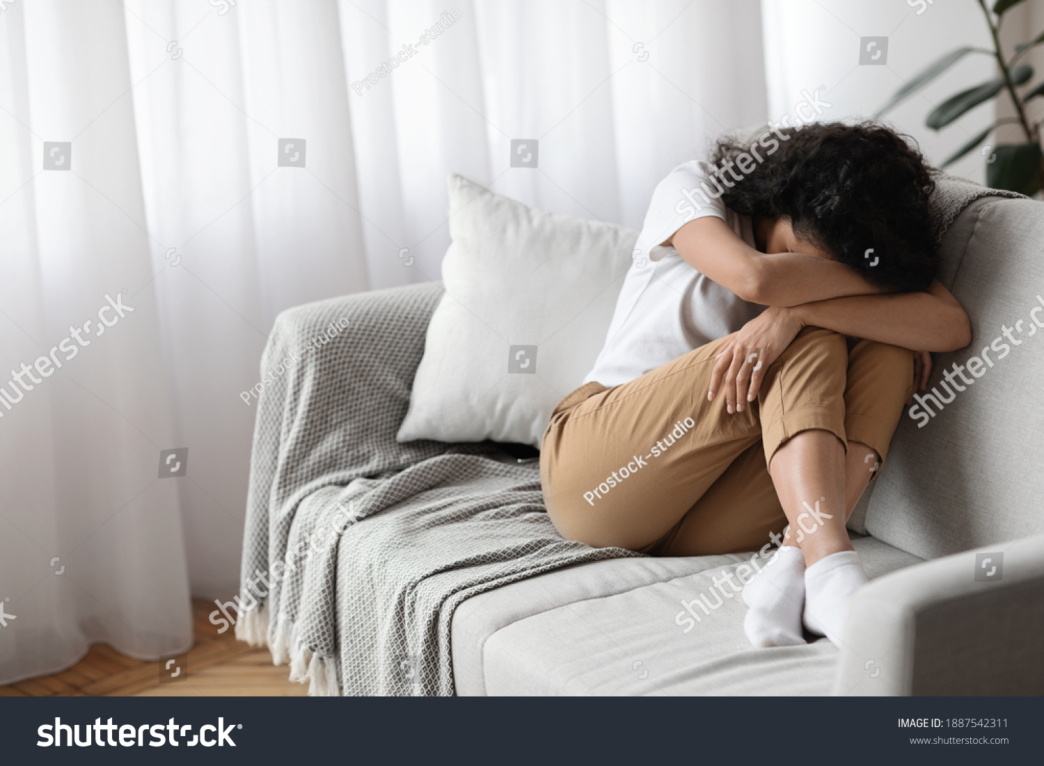 Depressed brunette woman sitting on couch at home alone, crying, suffering from loneliness during lockdown, copy space. Upset young lady having bad day, spending weekend on her own, feeling lonely #1887542311