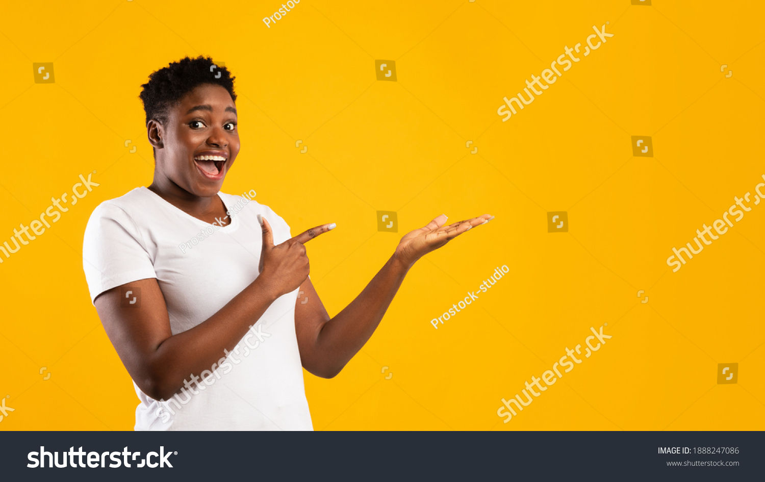 Excited Plus-Size Black Woman Showing Invisible Object Pointing Fingers Aside Advertising Your Text Posing Standing On Yellow Studio Background, Smiling To Camera. Blank Space, Panorama #1888247086