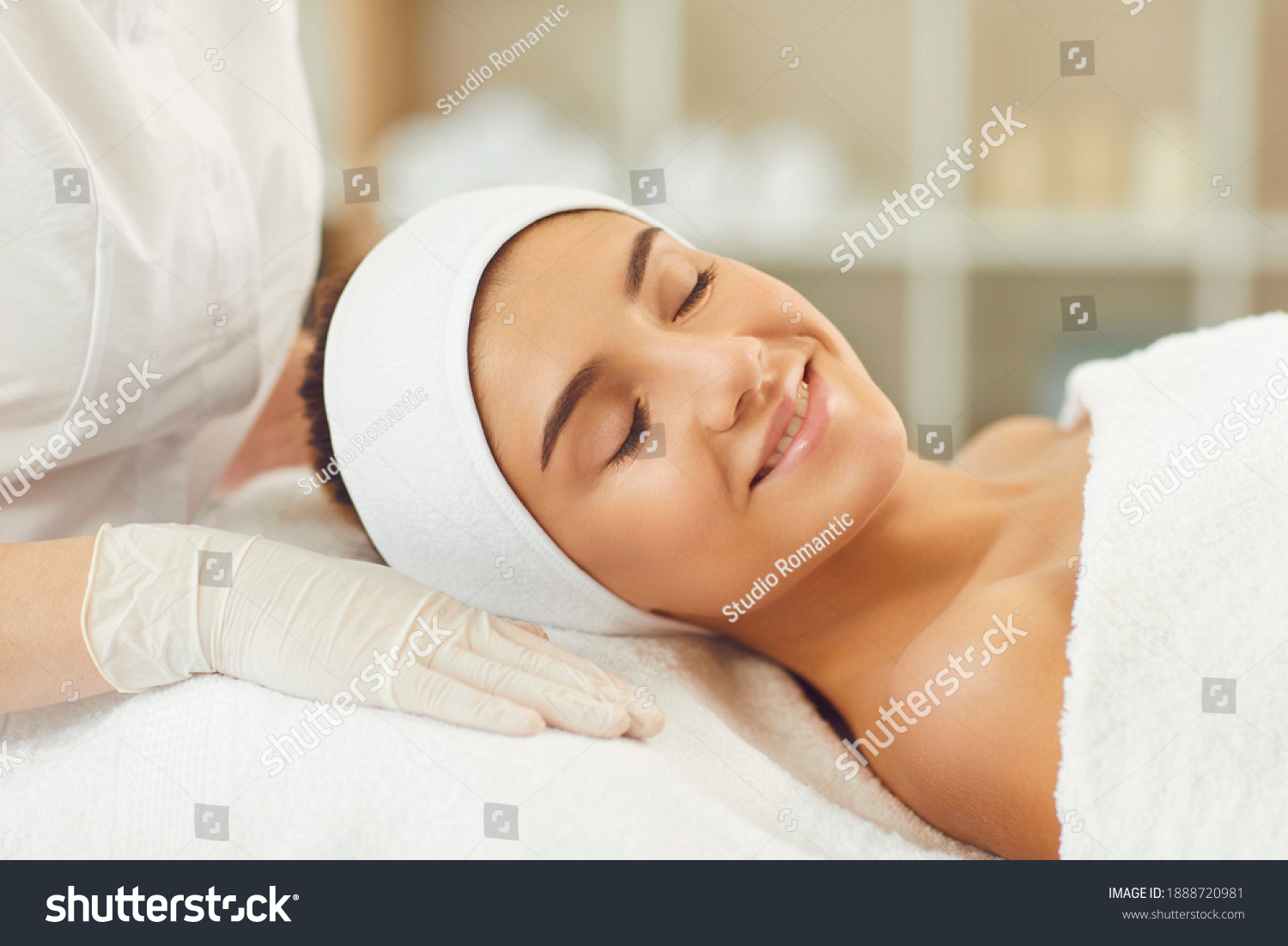 Beautiful young woman receiving skin treatment from a beautician. Smiling young womans face with clsed eyes expressing happiness during skincare procedure in beauty spa salon #1888720981