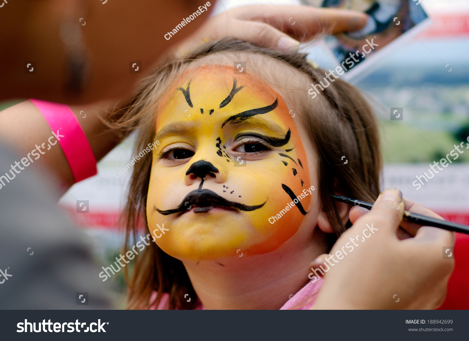 Young girl (female age 4-5) getting her face painted like a lion by a face painting make up artist on Halloween or Purim carnival Jewish holiday. Real people. Copy space #188942699