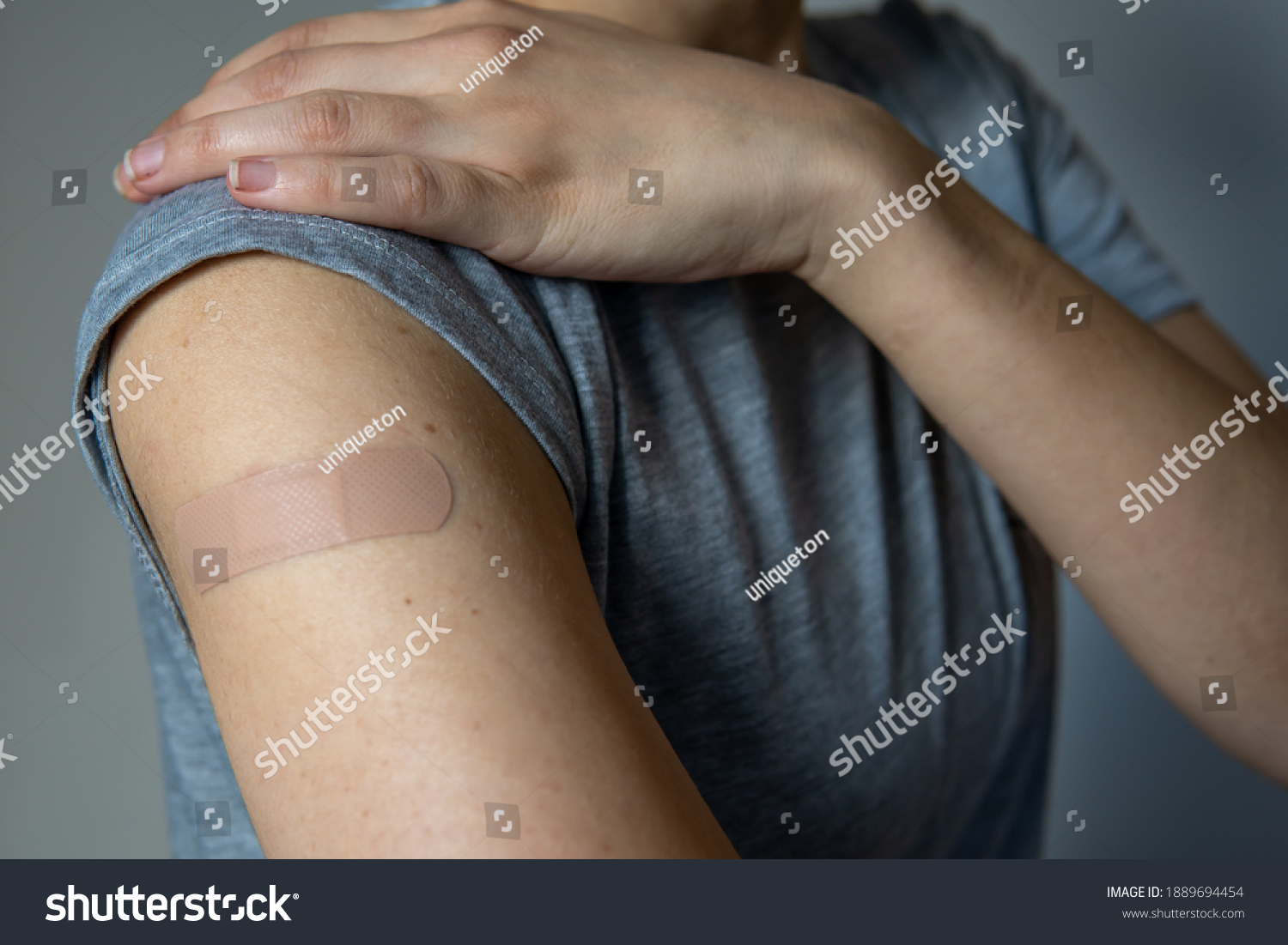 A woman showing her arm with an adhesive bandage after injection of vaccine or a scratch on the skin. First aid. Medical, pharmacy, and healthcare concept. After vaccination treatment. #1889694454
