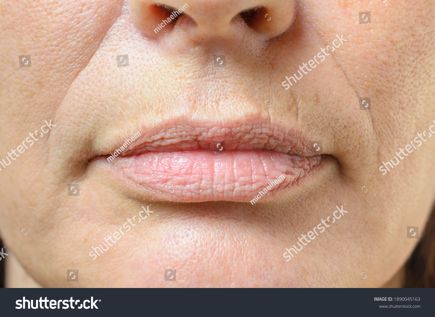Closeup on the mouth of a middle-aged brunette woman with her mouth closed and a serious expression #1890045163