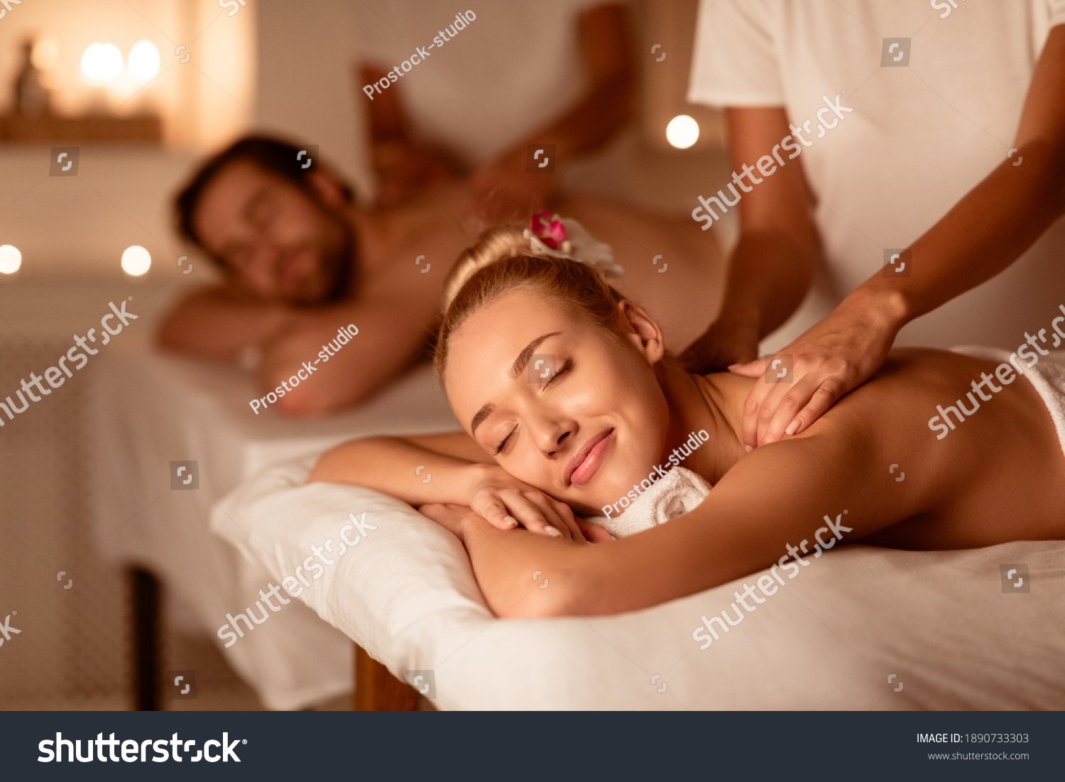 Couple Relaxing Receiving Back Massage Lying Closing Eyes At Romantic Luxury Spa With Burning Candles And Flowers. Wellness And Body Relaxation Therapy. Selective Focus, Low Light #1890733303