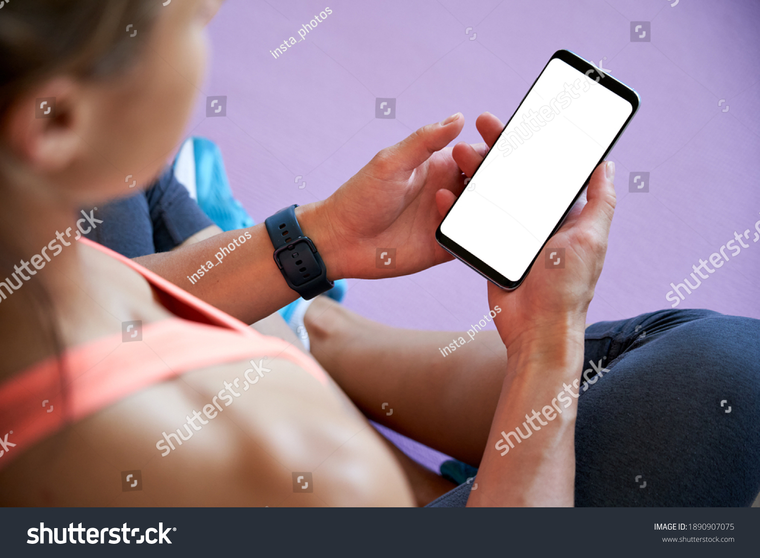 Over shoulder closeup view of fit sporty woman yoga teacher sit on mat holding phone mock up screen video calling, watching online workout training class video, using fitness app at home in gym. #1890907075