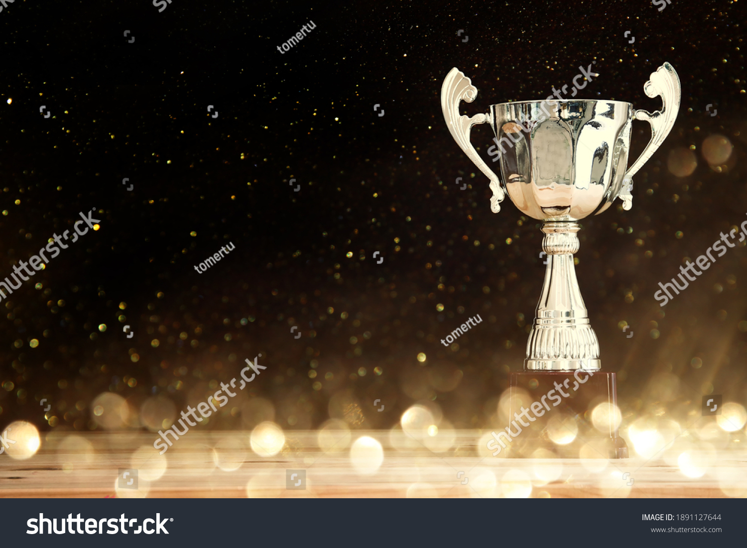 image of silver trophy over wooden table and dark background, with abstract shiny lights #1891127644