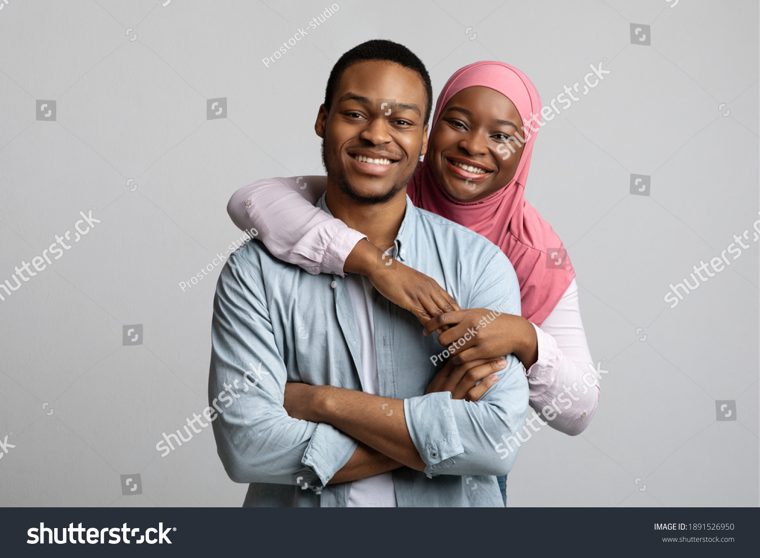 Portrait of loving african american young muslim couple posing on grey studio background. Beautiful black man and woman in hijab hugging and smiling at camera, relationships concept #1891526950