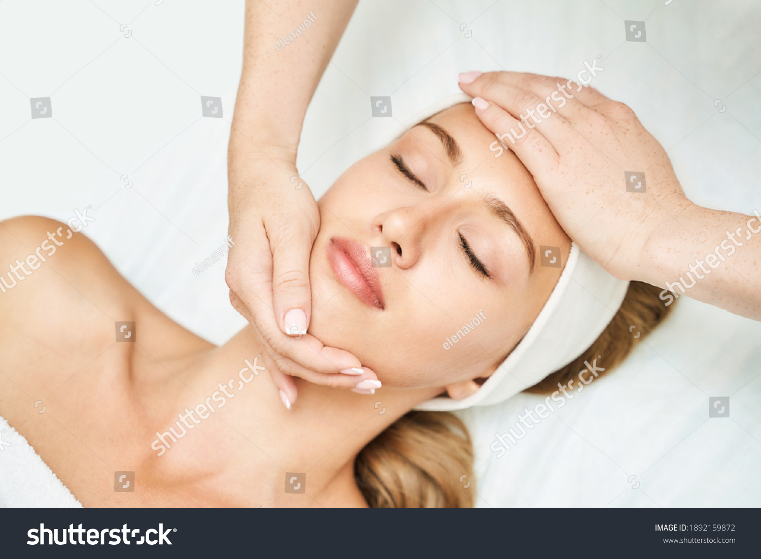 Face massage at spa salon. Doctor hands. Pretty female patient. Beauty treatment. Healthy skin procedure. Young woman head. Light background. Scrub rejuvenation. Facial dermatology mask. Detox therapy #1892159872