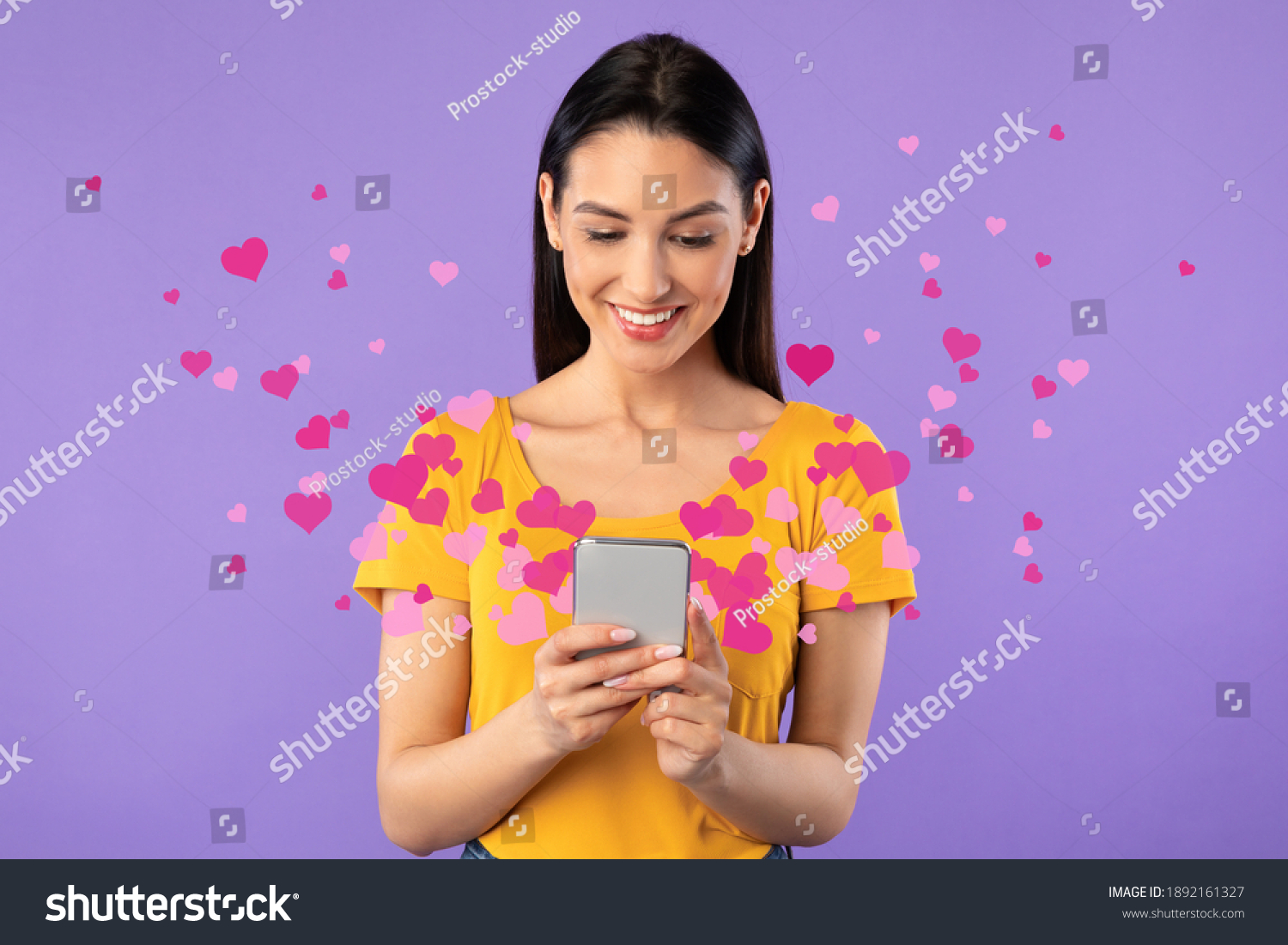 Love Mail Concept. Smiling young woman using smartphone, receiving love text message with pink hearts flying away from gadget screen isolated on purple studio background. Dating App. #1892161327