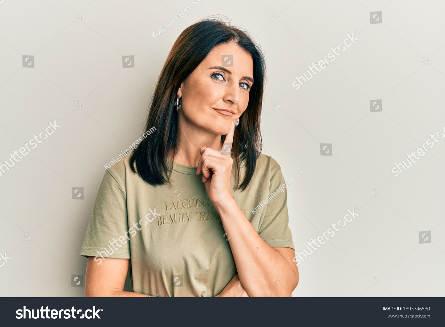 Middle age brunette woman wearing casual clothes smiling looking confident at the camera with crossed arms and hand on chin. thinking positive.  #1893746530