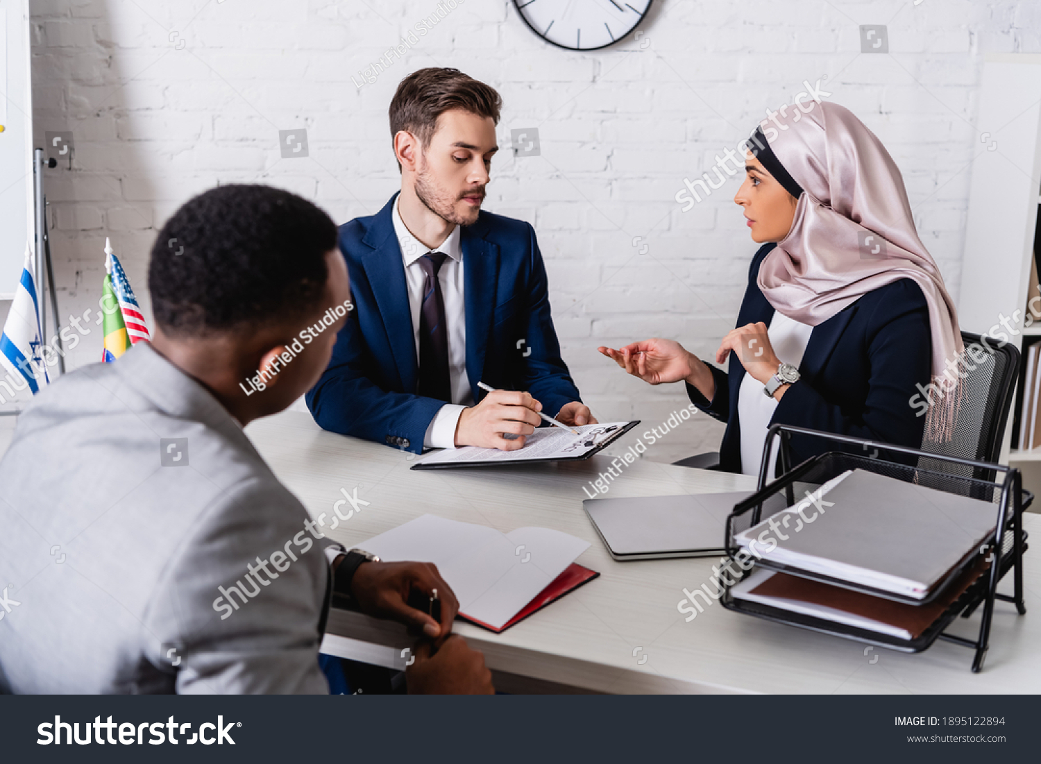 businessman pointing with pen at contract near arabian businesswoman and interpreter, blurred foreground #1895122894