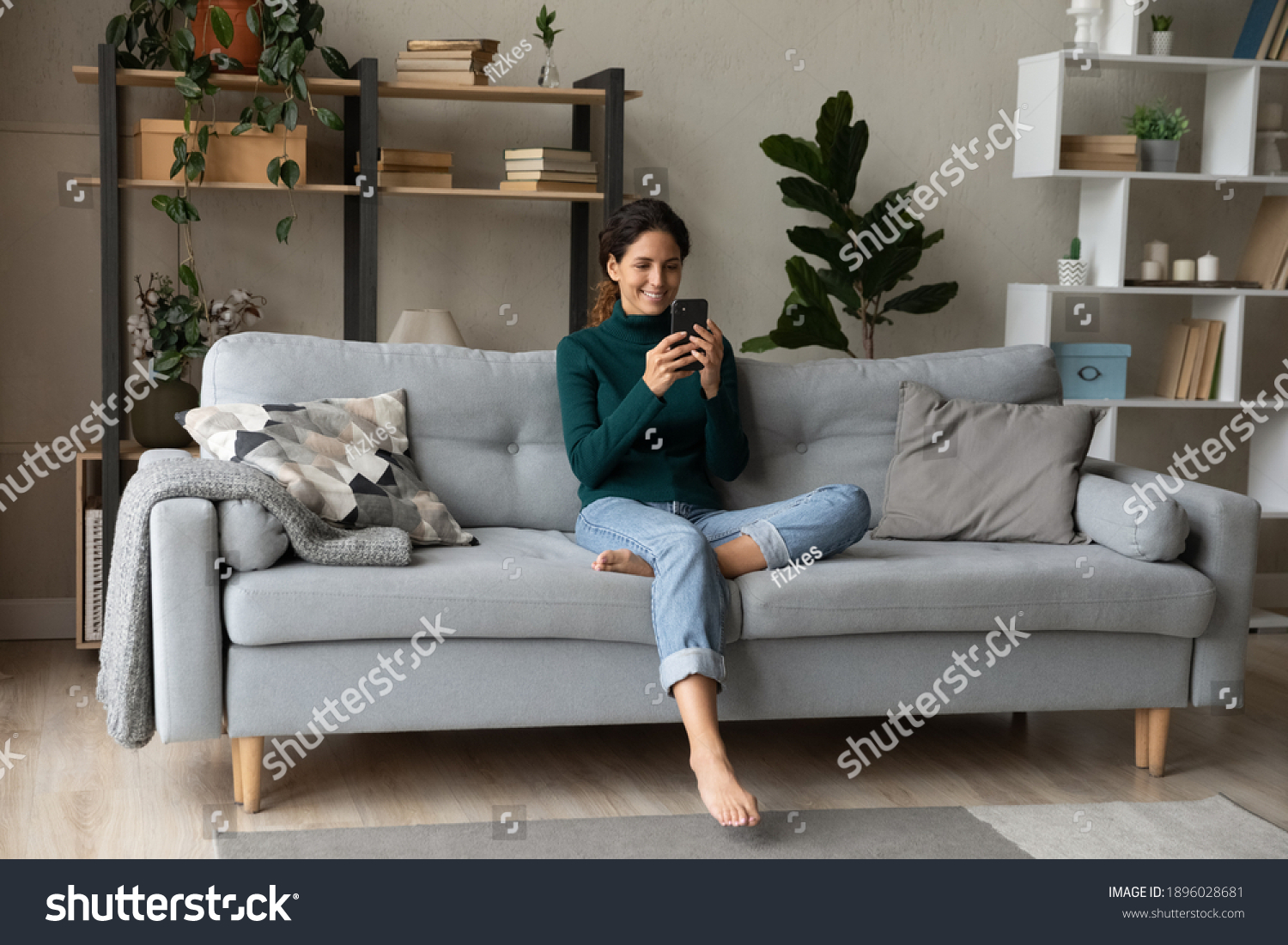 Smiling young Caucasian woman sit relax on couch in living room talk on video call. Happy millennial female rest on sofa at home have webcam digital virtual communication on cellphone. #1896028681