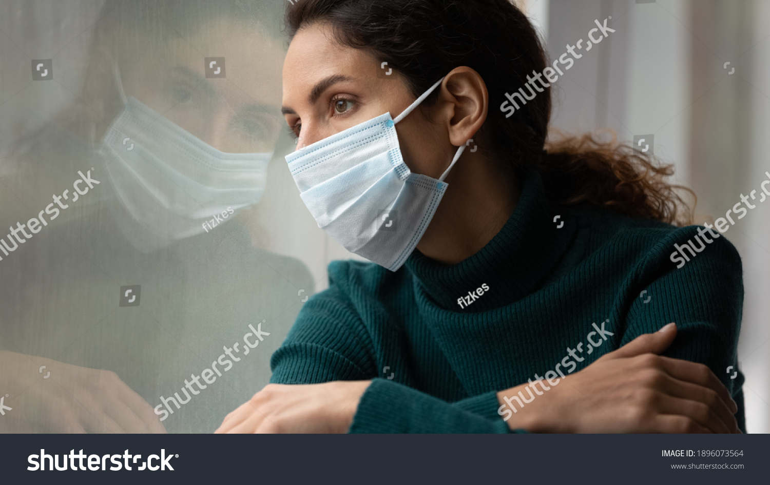 Upset young Caucasian woman in medical facial mask look in window feel lonely distressed sick with covid-19. Unhappy female in facemask suffer from coronavirus. Quarantine, corona pandemic concept. #1896073564