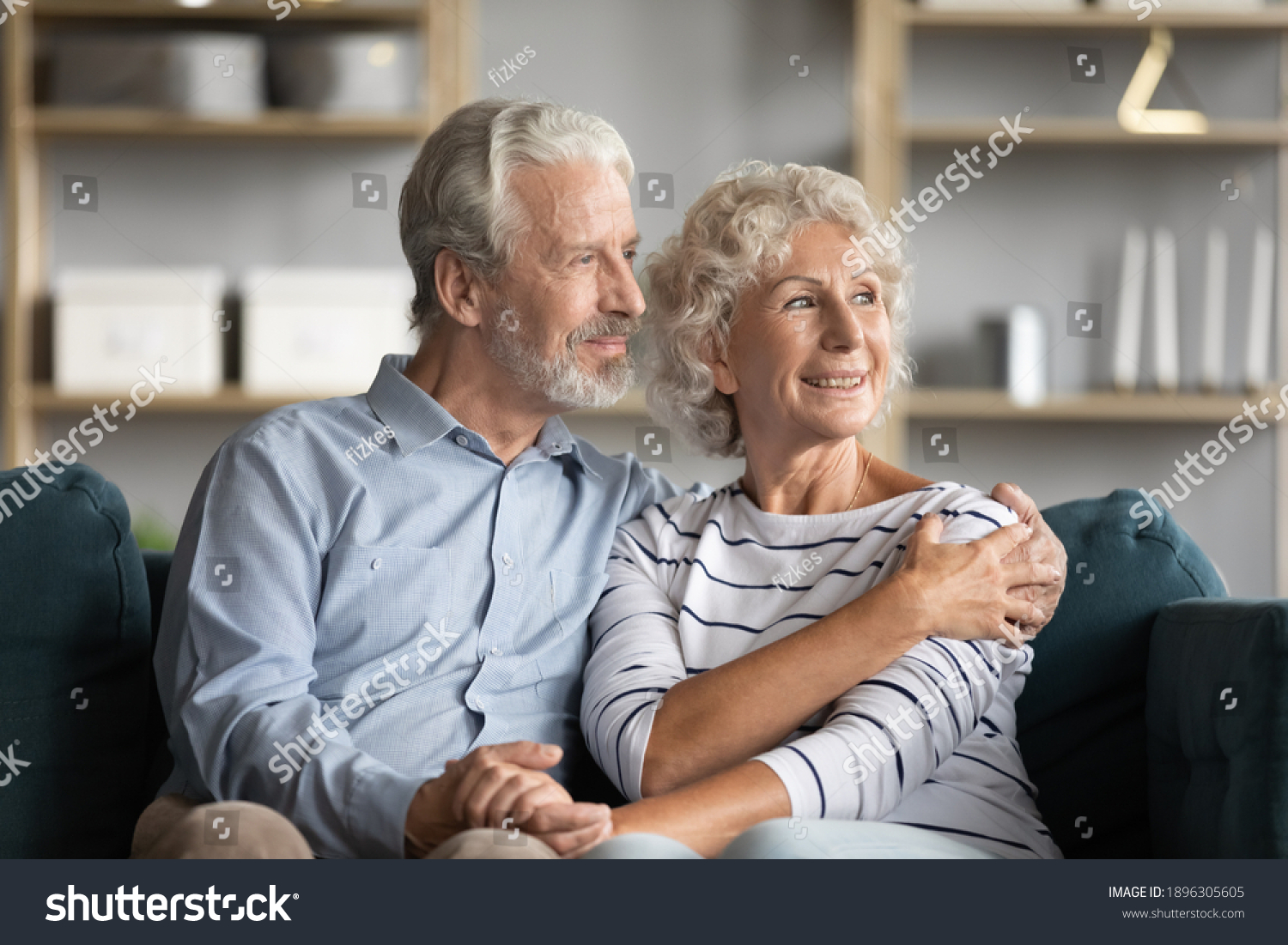 Dreamy middle aged senior loving retired family couple looking in distance, planning common future or recollecting memories, enjoying peaceful moment relaxing together on cozy sofa in living room. #1896305605