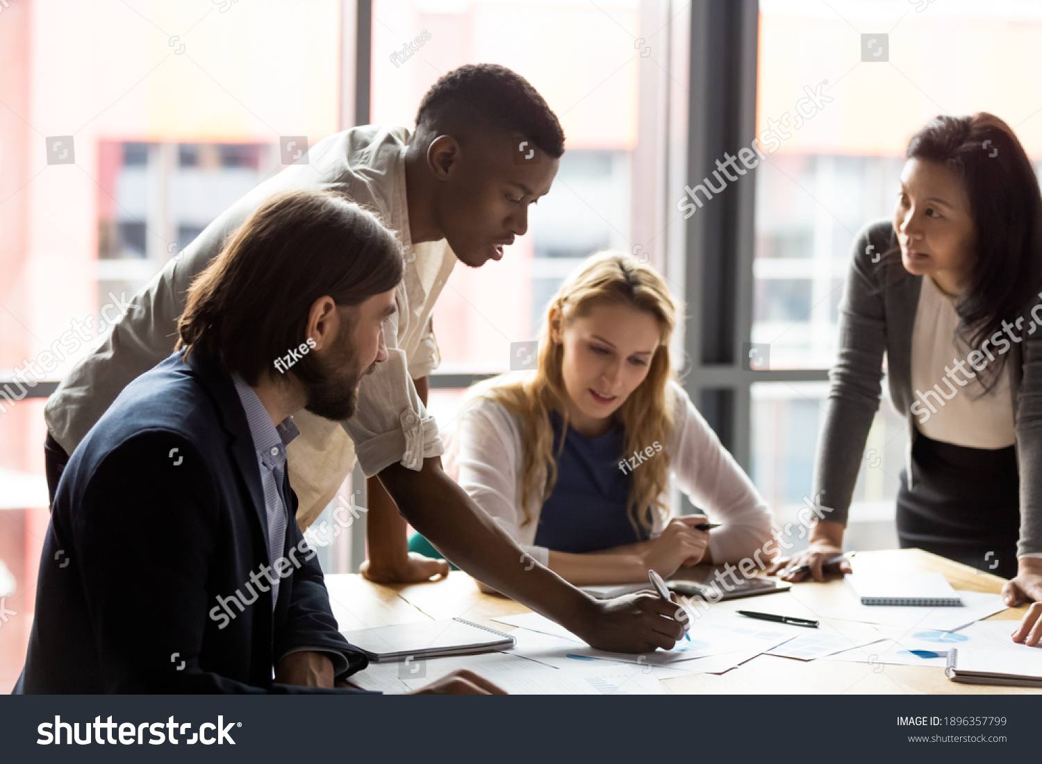 Concentrated young african american employee analyzing marketing research results or sales statistics data at briefing meeting with motivated older korean and young caucasian colleagues in office. #1896357799