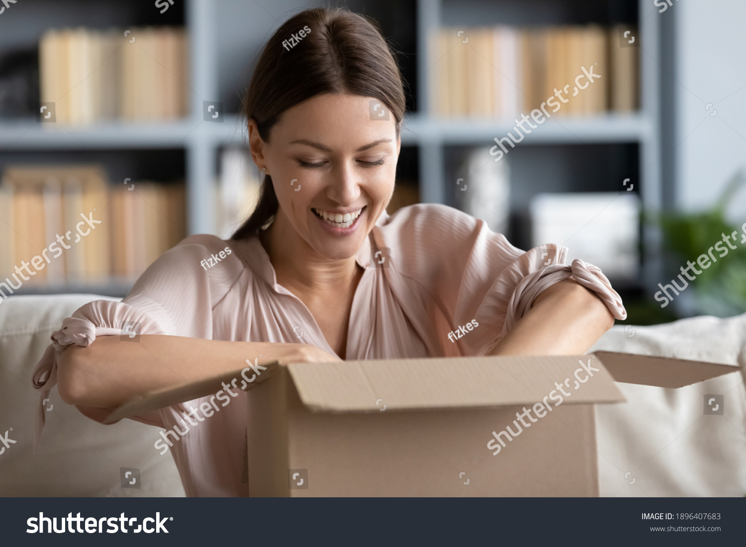 Close up overjoyed young woman unpacking cardboard box at home, satisfied customer received awaited parcel with online store order, sitting on couch, good quick delivery service concept #1896407683
