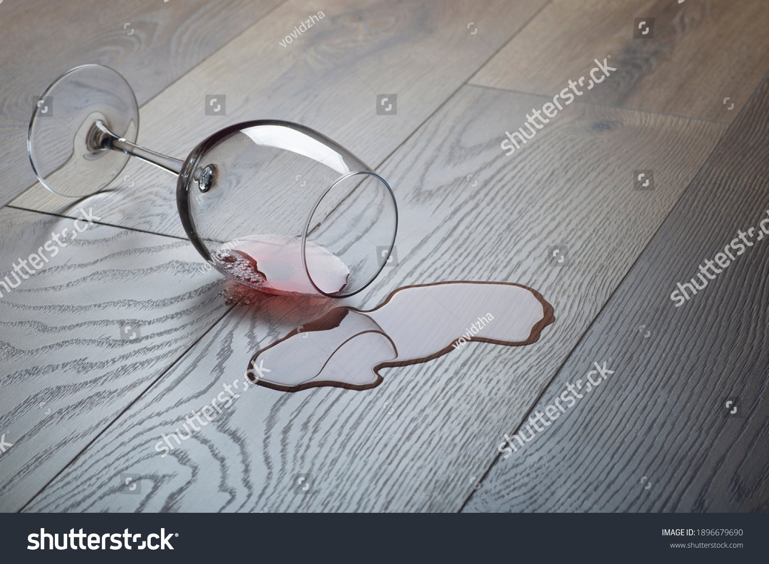 Wooden floor with overturned glass of red wine. Spilled wine on a wooden laminate (parquet) floor with moisture protection. Concept of alcoholism, broken relationships, depression #1896679690