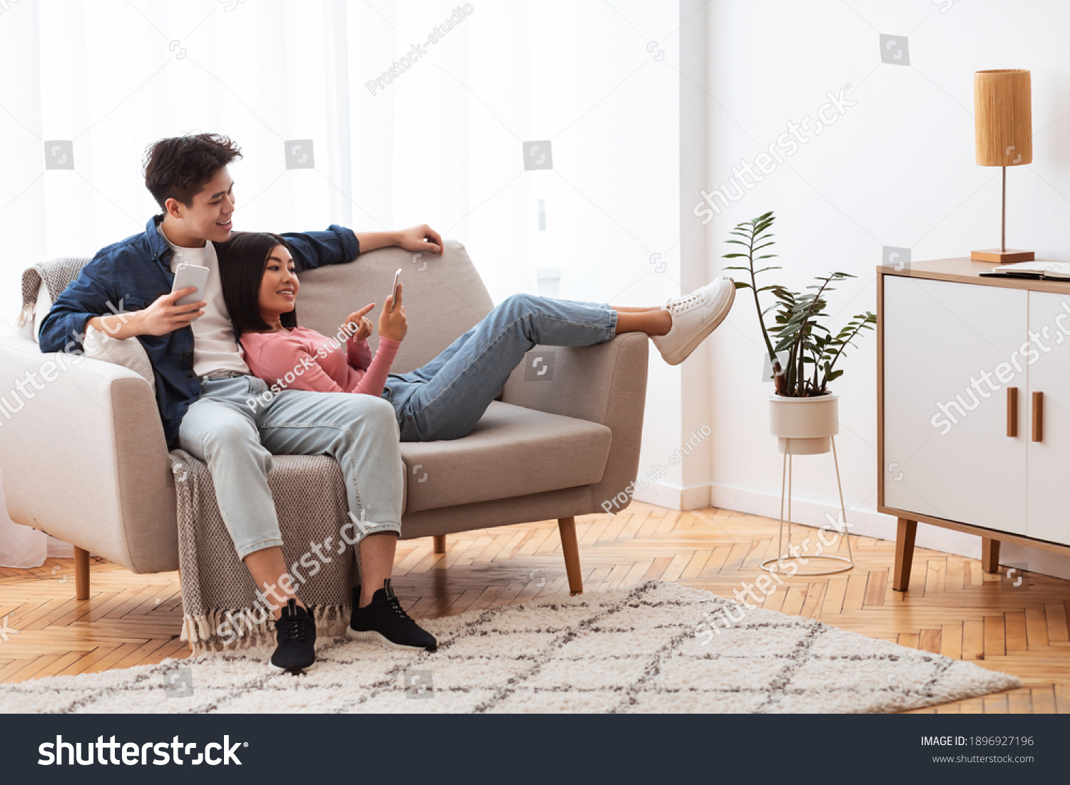 Japanese Couple Using Cellphones Texting And Browsing Internet Relaxing Sitting On Couch Indoor. Weekend Leisure. Happy And Relaxed Asian Family Using Mobile Application Resting At Home #1896927196