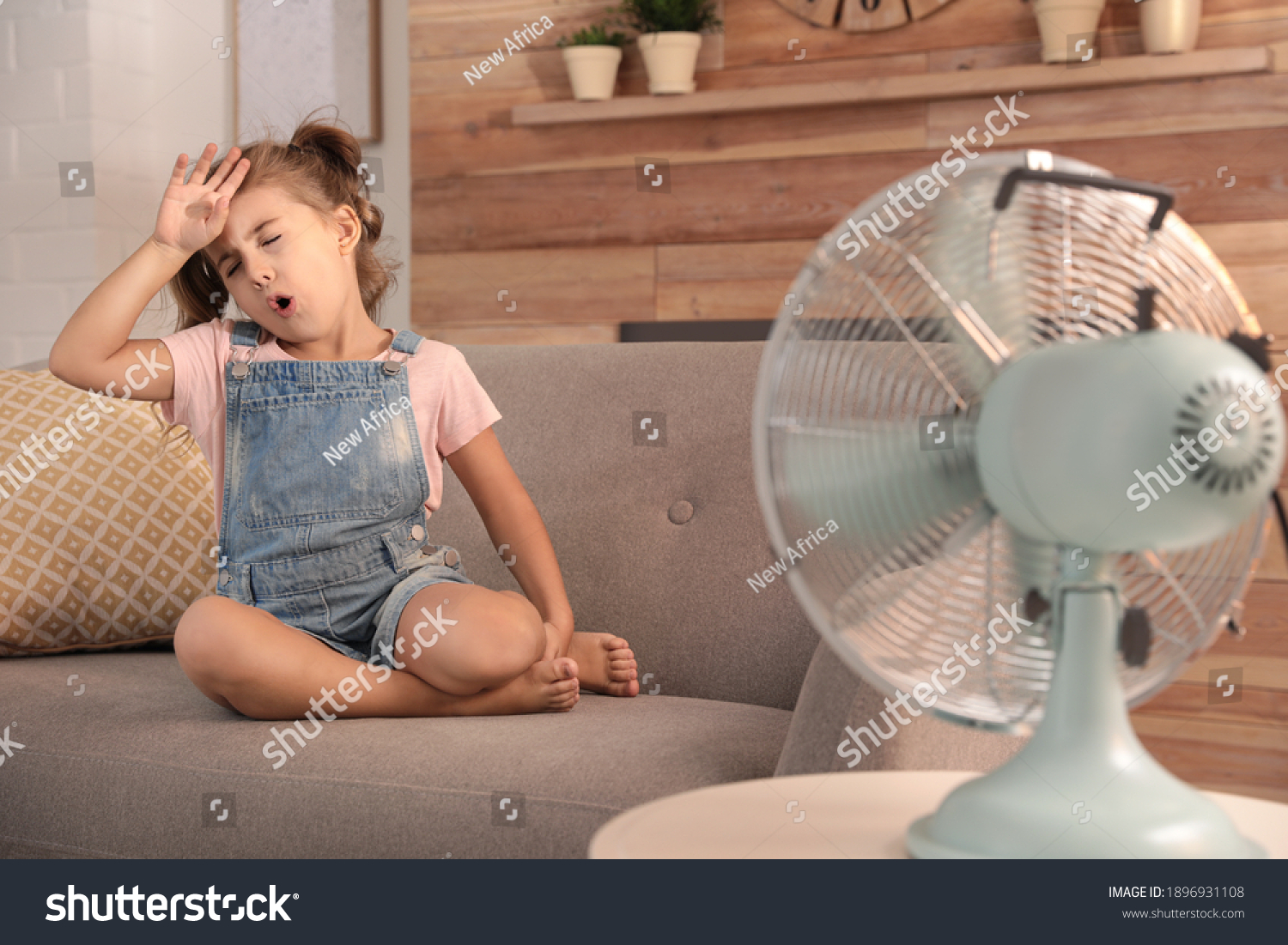 Little girl enjoying air flow from fan on sofa in living room. Summer heat #1896931108