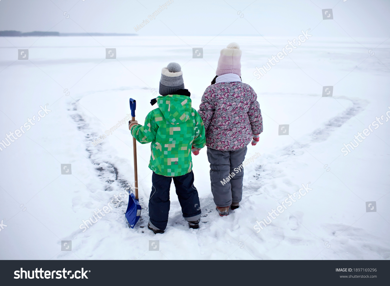 Boy and girl have fun and removing snow from the ice on the frozen lake in heart shape. Winter romantic, silence and wild nature, active winter weekend, outdoor activities, icy landscape, lifestyle #1897169296