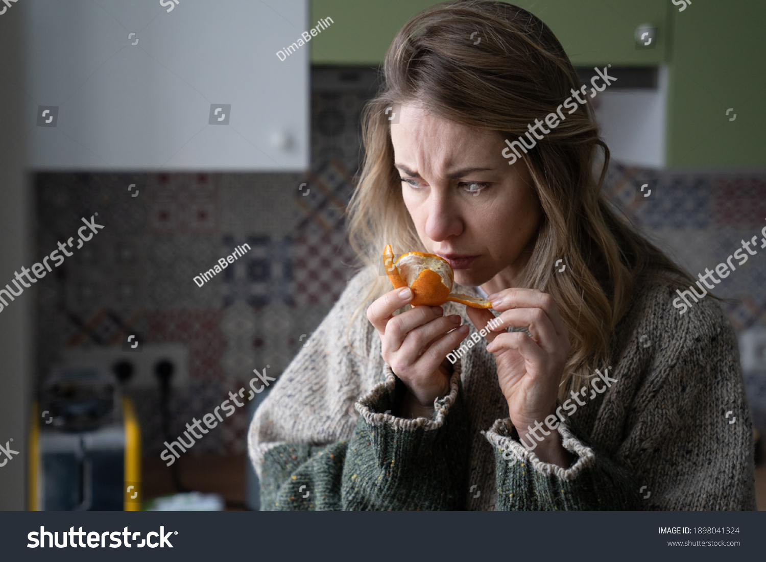 Sick woman trying to sense smell of fresh tangerine orange, has symptoms of Covid-19, corona virus infection - loss of smell and taste, standing at home. One of the main signs of the disease. #1898041324