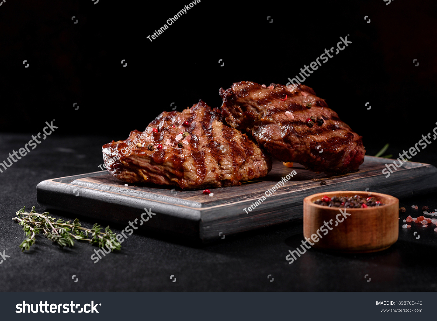 Fresh juicy delicious beef steak on a dark background. Meat dish with spices and herbs #1898765446