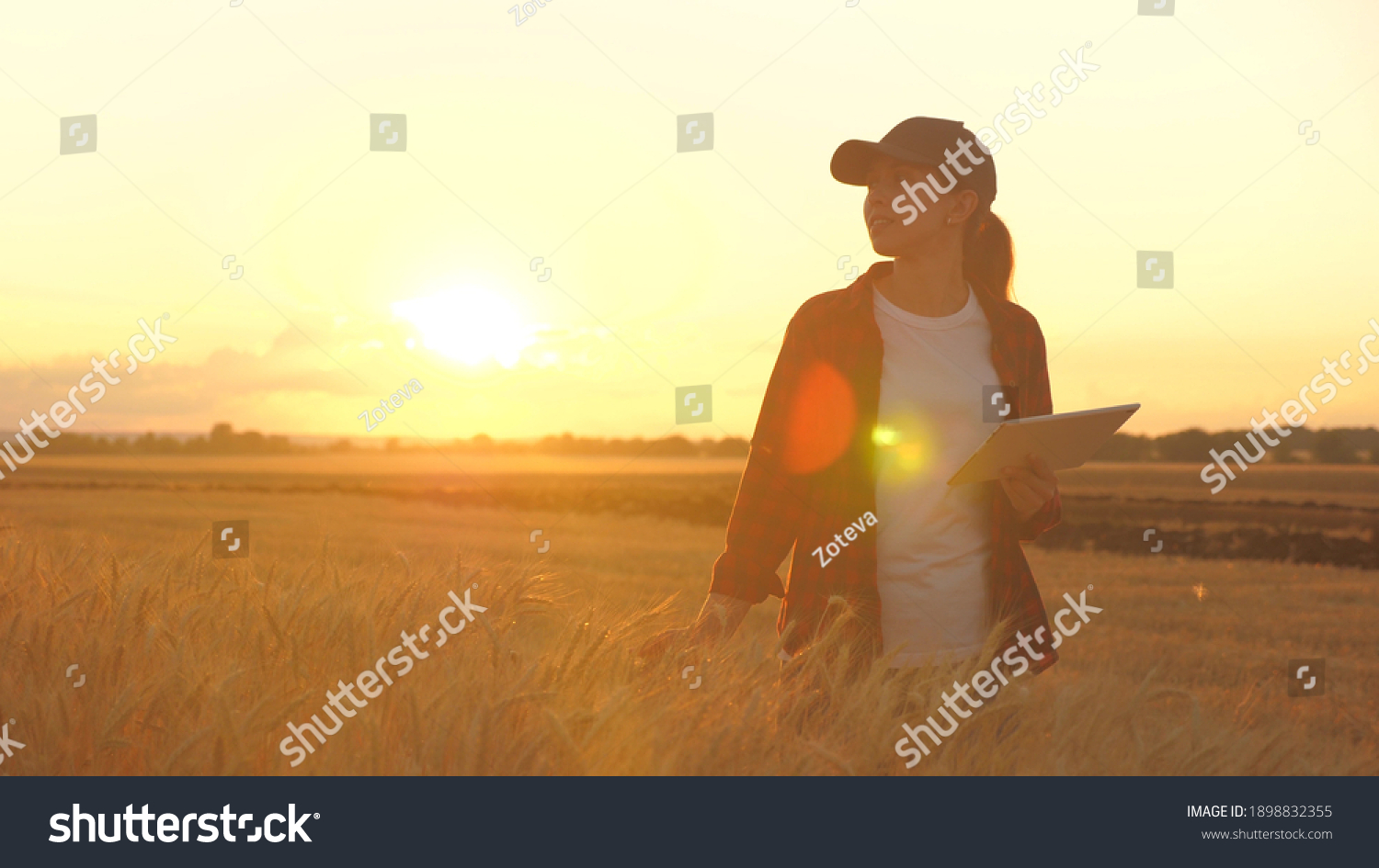 Agronomist woman farmer, business woman looks into a tablet in a wheat field. Modern technologists and gadgets in agriculture. Business woman working in the field. Farmer in wheat field at sunset. #1898832355