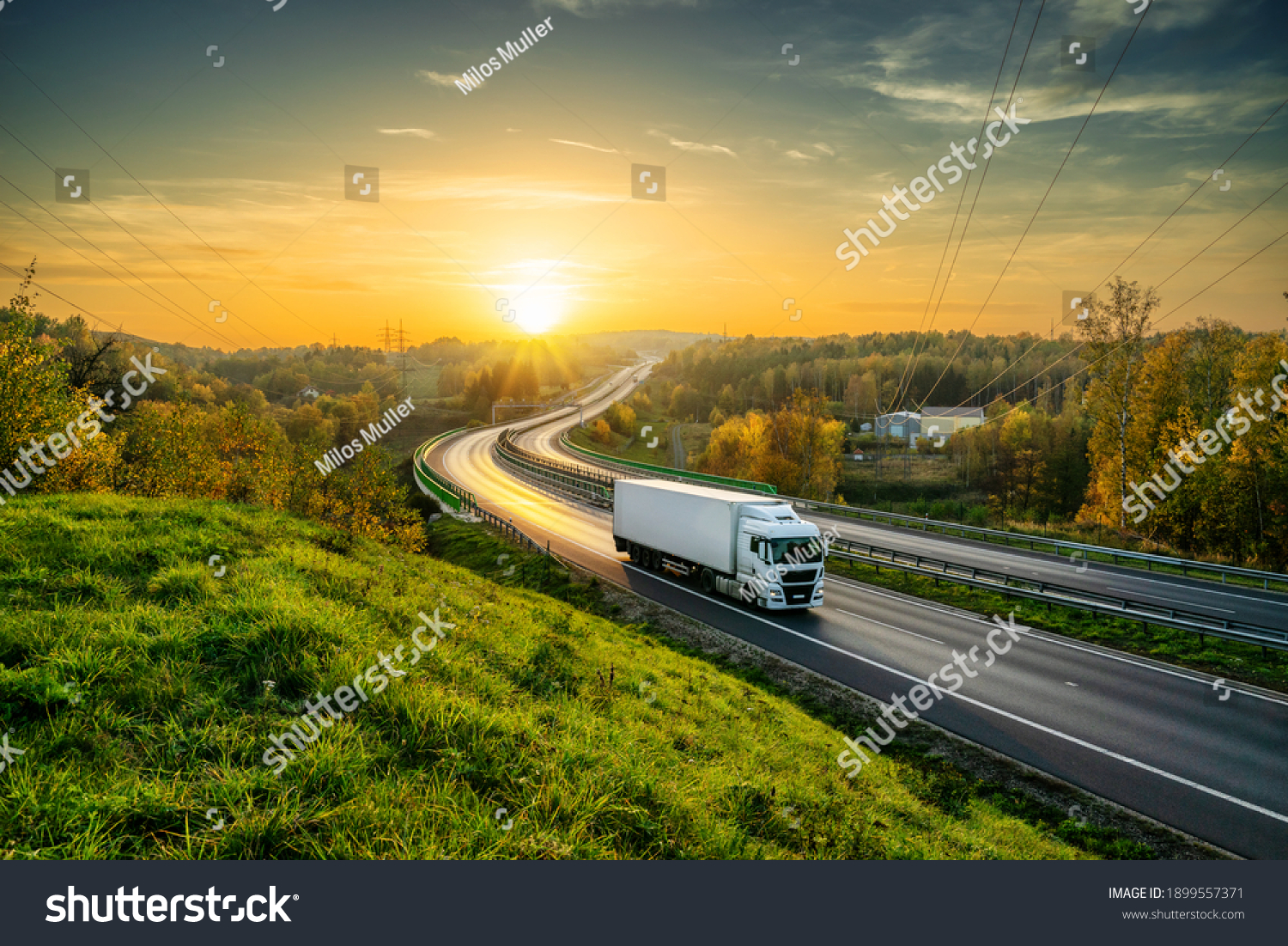 White truck driving on the highway winding through forested landscape in autumn colors at sunset #1899557371