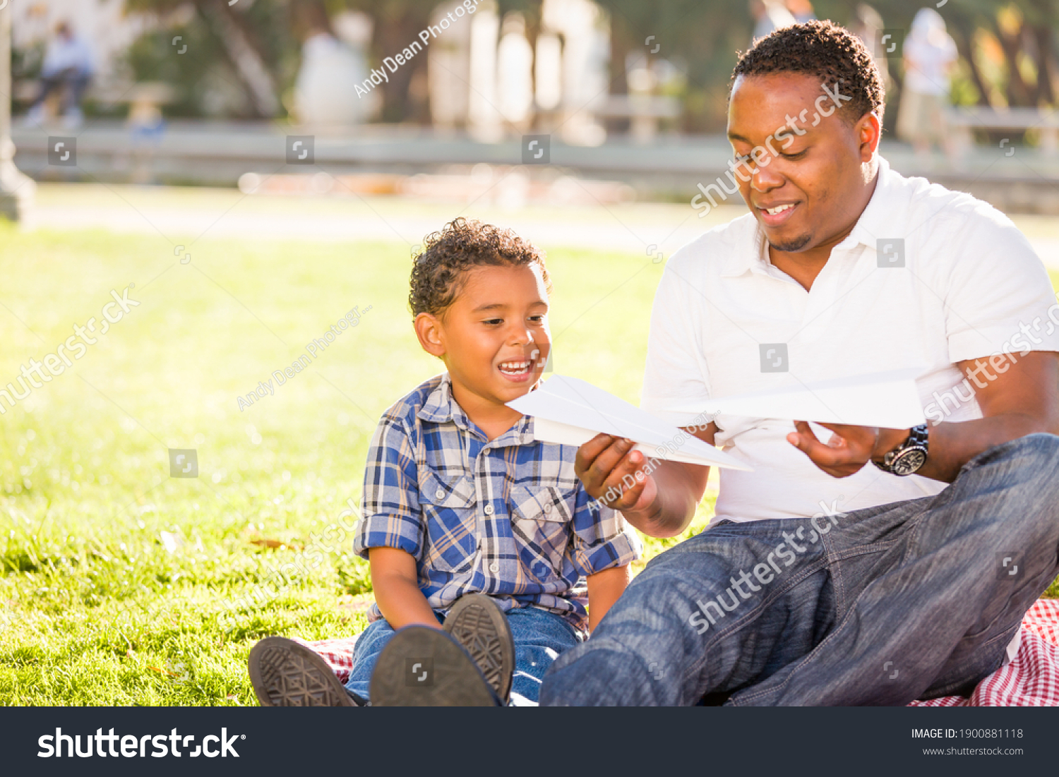 Happy African American Father and Mixed Race Son Playing with Paper Airplanes in the Park #1900881118
