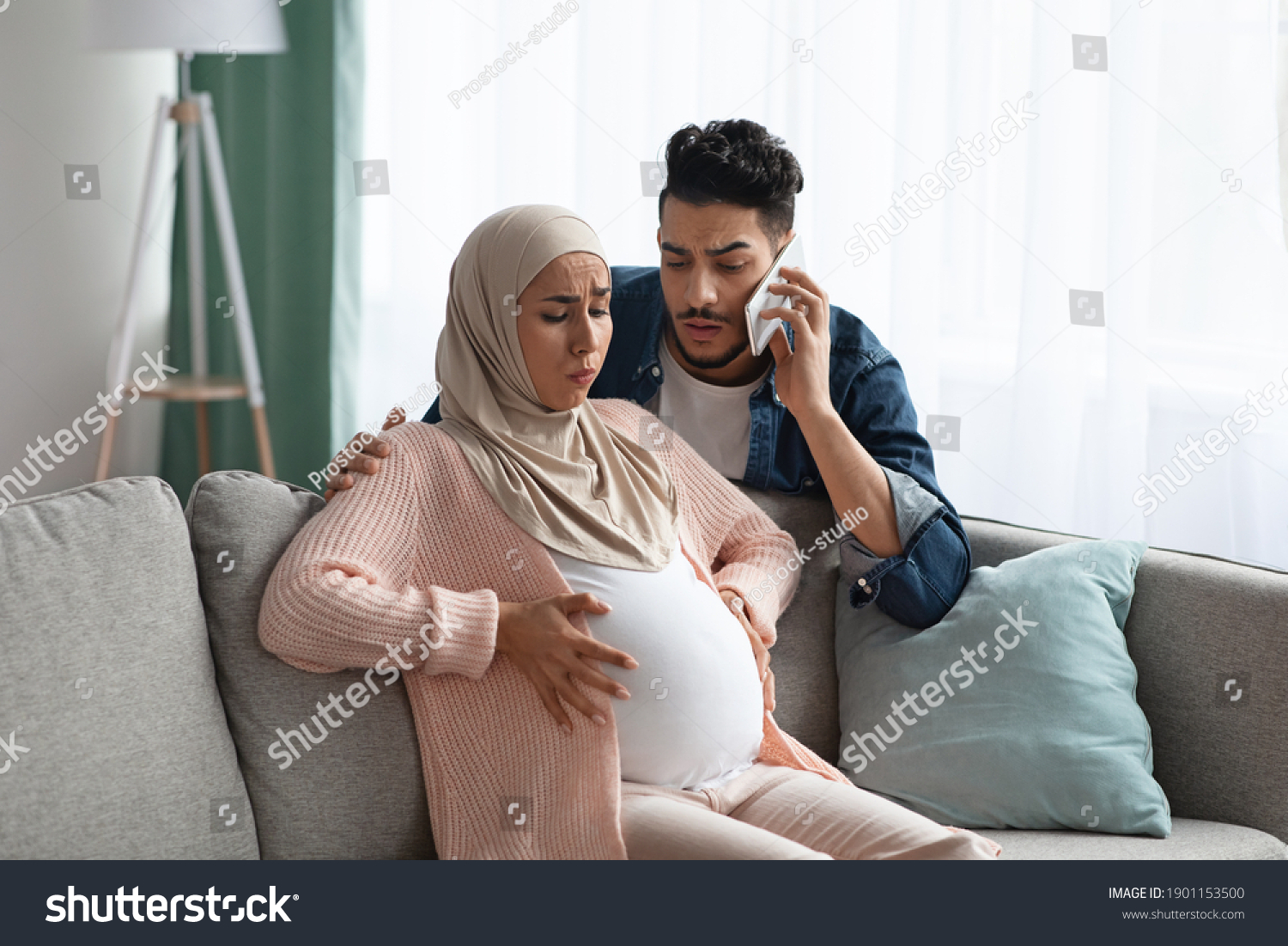 Worry Muslim Husband Calling Emergency While His Pregnant Wife Having Prenatal Contractions At Home. Islamic Expecting Mother In Hijab Suffering Painful Spasms And Spontaneous Labour, Copy Space #1901153500
