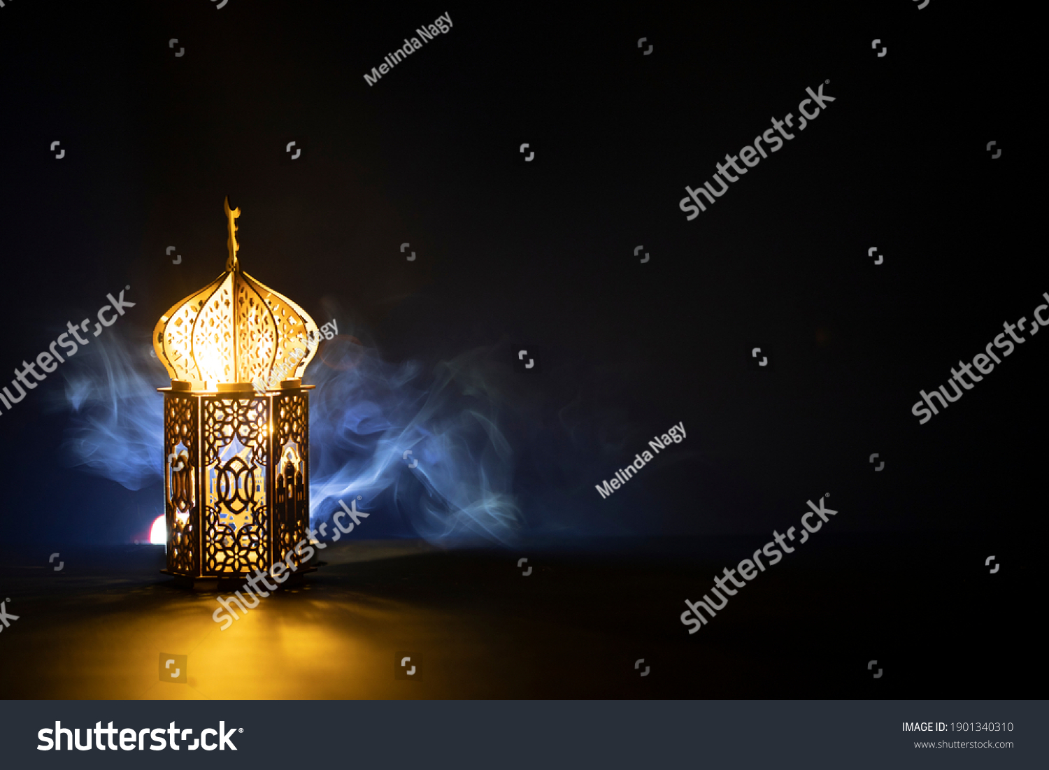 Ornamental Arabic lantern with burning candle glowing at night and glittering golden bokeh lights. Festive greeting card for Muslim holy month Ramadan Kareem. #1901340310