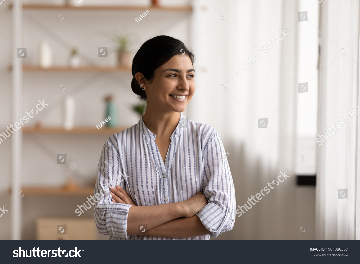 Successful millennial indian lady stand at home keep arms crossed on chest look at window with confident smile. Happy mixed race female private enterpreneur proud of being self made business woman #1901388307