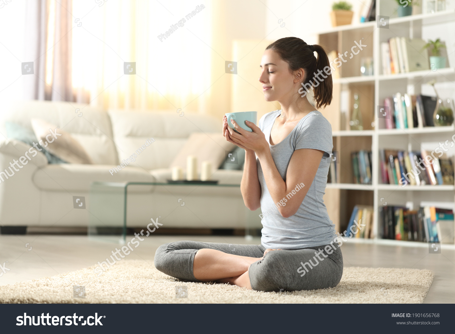 Yogi drinking tea after yoga exercises sitting on the floor at home #1901656768