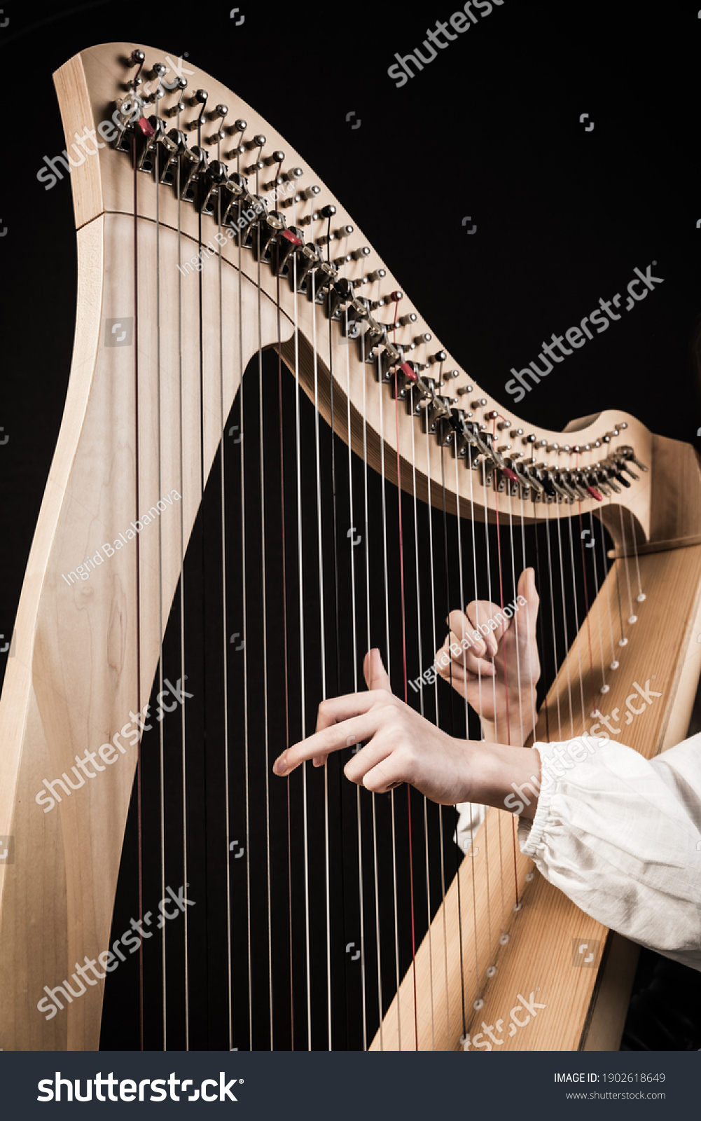 Hands playing wooden harp on black background #1902618649