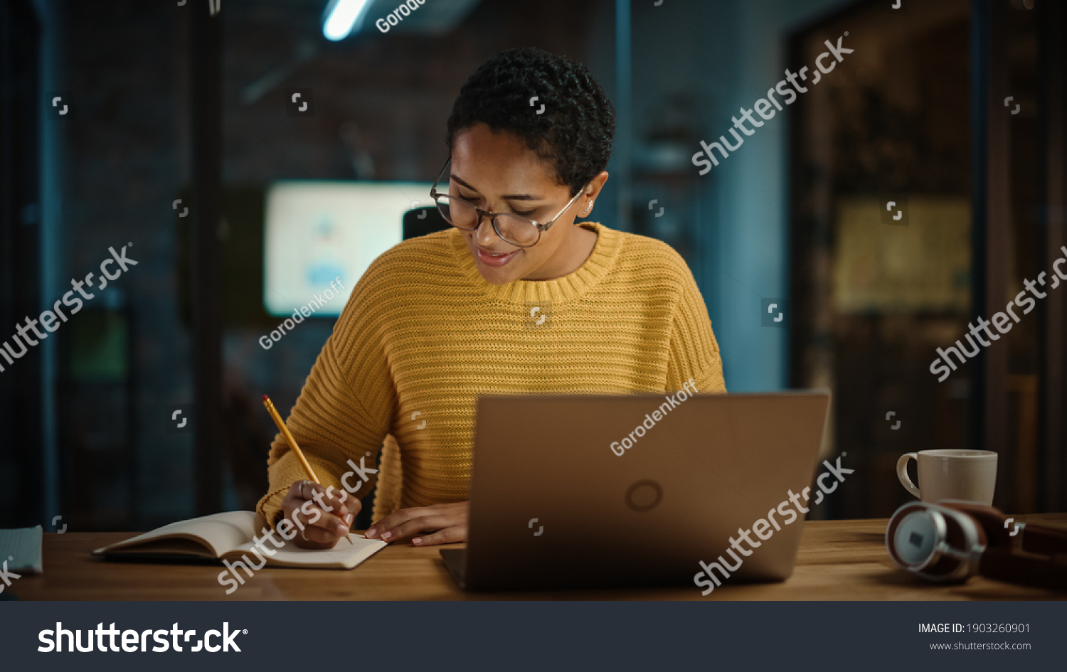 Young Hispanic Marketing Specialist Working on Laptop Computer in Busy Creative Office Environment. Beautiful Diverse Multiethnic Female Project Manager is Writing Down Notes in Paper Notebook. #1903260901