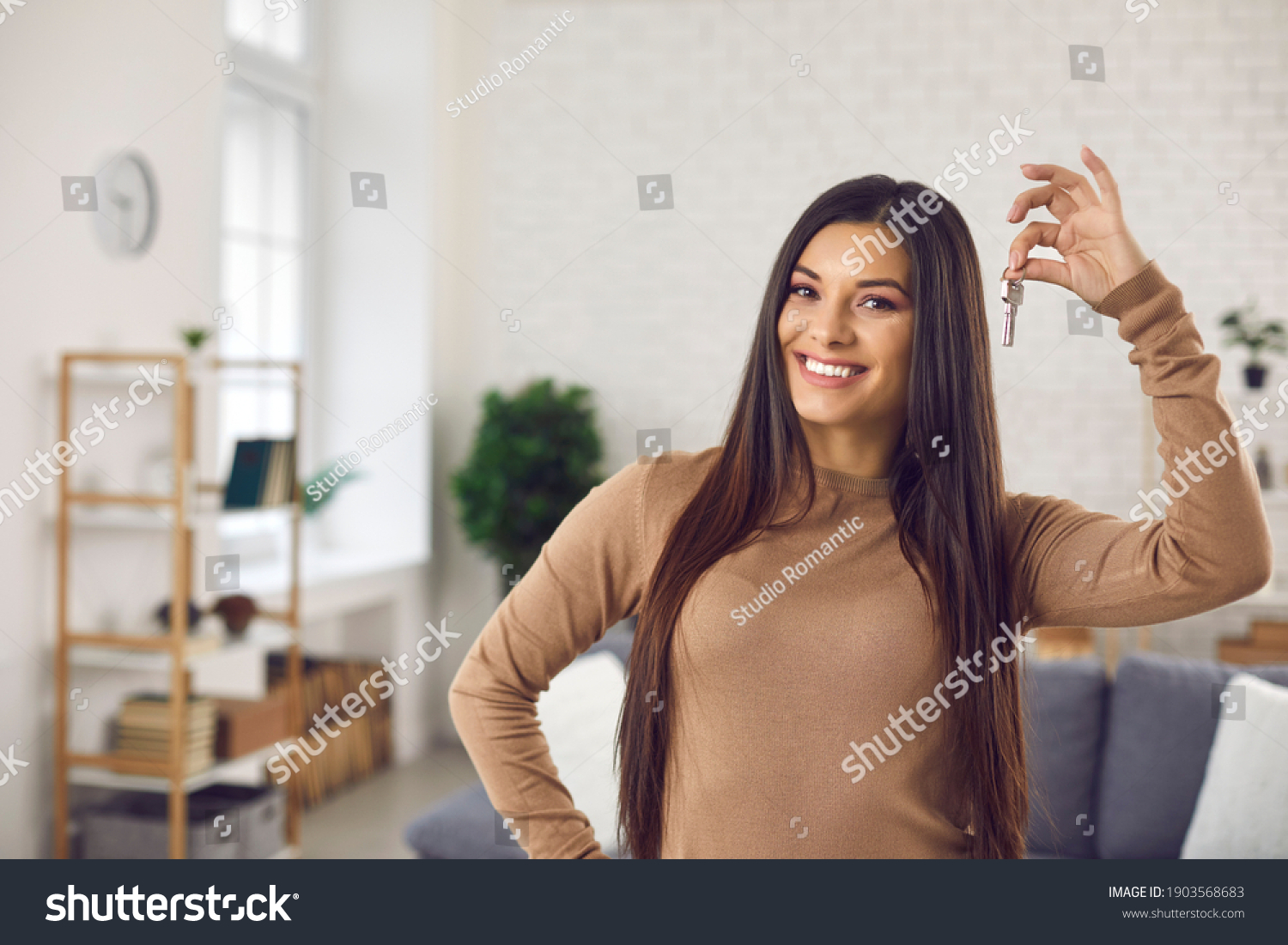 Happy woman holding keys to new home, looking at camera and smiling. Portrait of first time buyer, house owner, apartment renter, flat tenant or landlady. Moving day and buying own property concept #1903568683