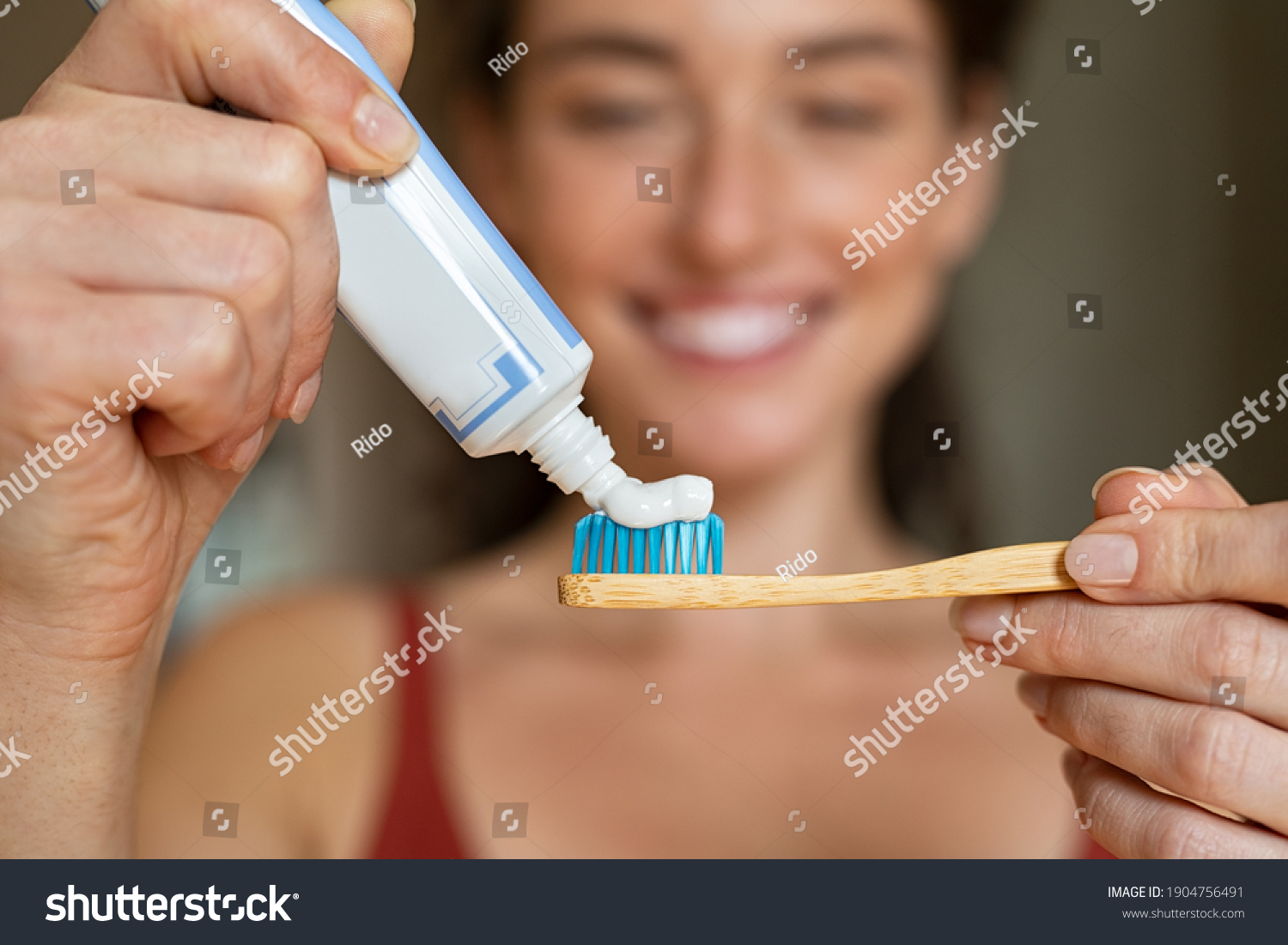 Close up of woman with tooth brush applying paste in bathroom. Closeup of girl hands squeezing toothpaste on ecological wooden brush. Smiling woman applying toothpaste on eco friendly toothbrush. #1904756491