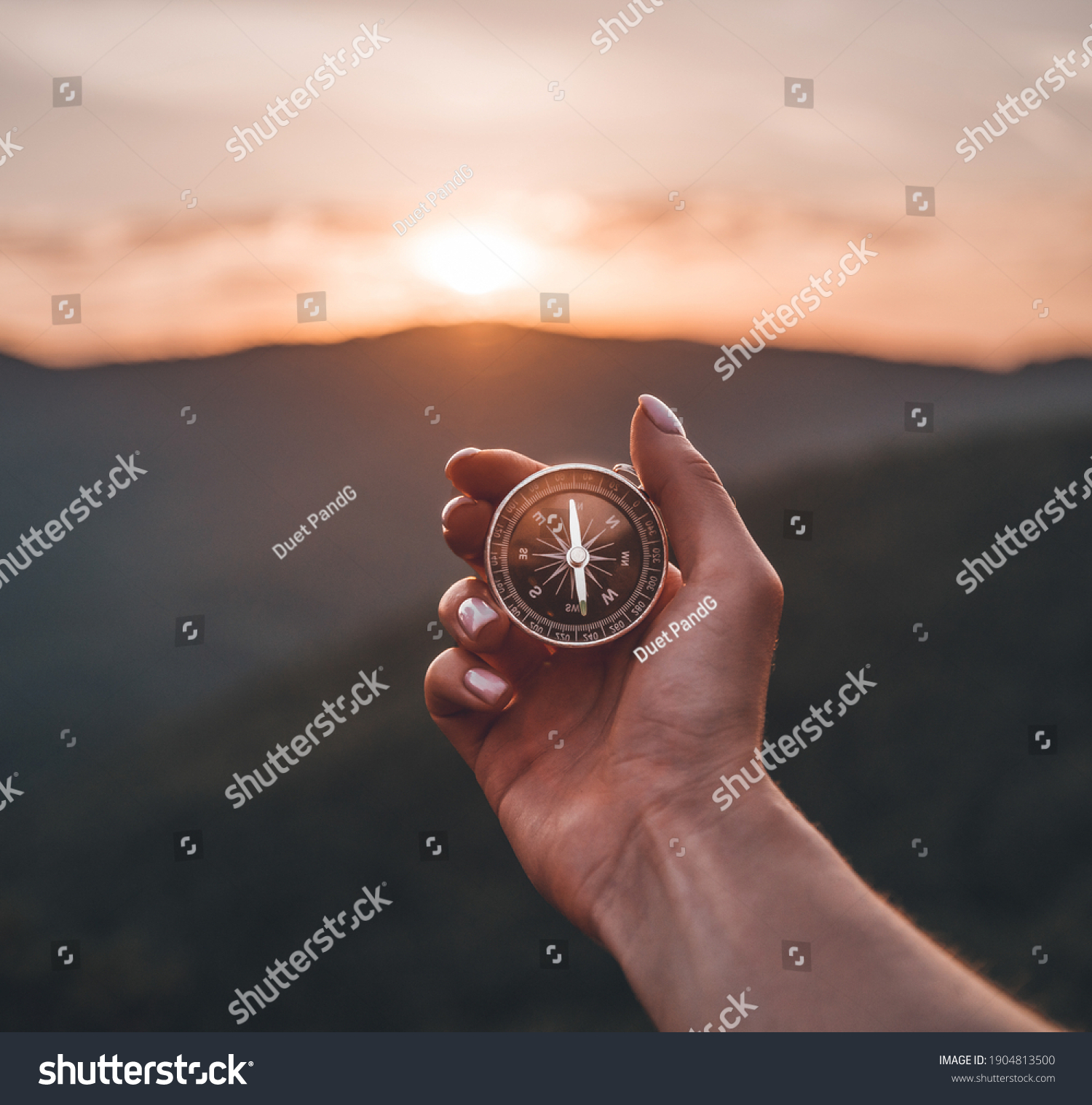 Traveler explorer young woman holding compass in a hand in summer mountains at sunrise, point of view. #1904813500