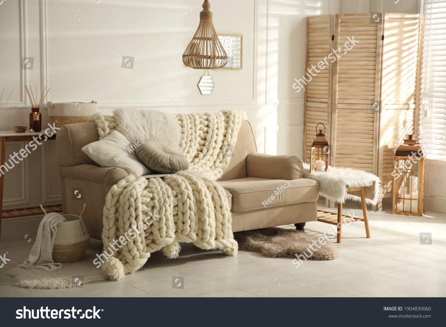 Cozy living room interior with beige sofa, knitted blanket and cushions #1904839060
