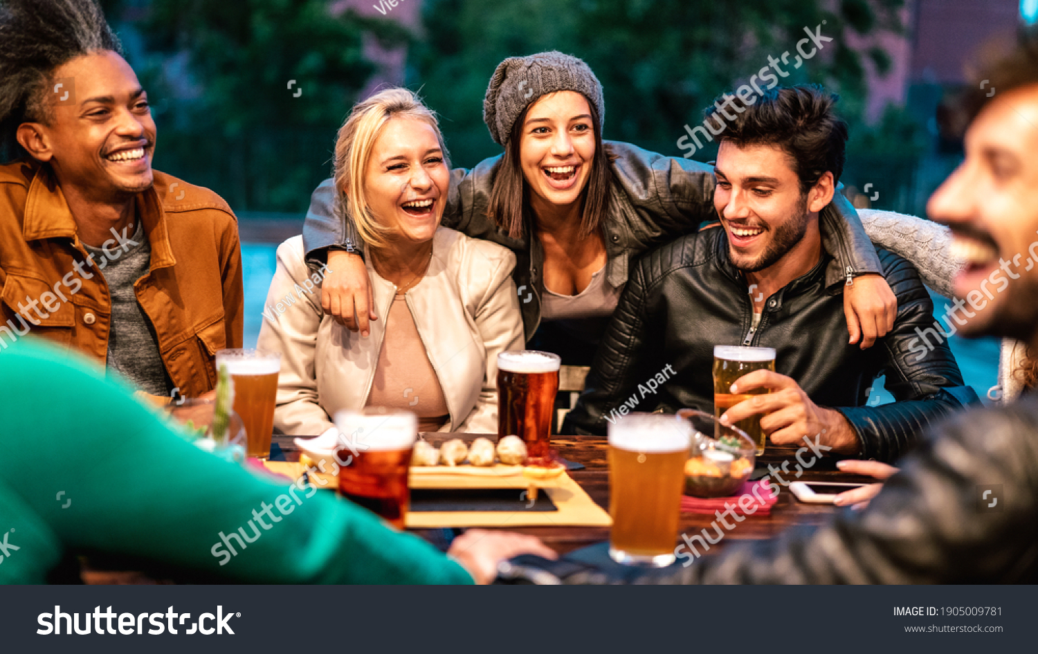 Happy friends drinking beer at brewery bar dehor - Friendship lifestyle concept with young milenial people enjoying time together at open air pub - Warm color tones on vivid filter with focus on girls #1905009781