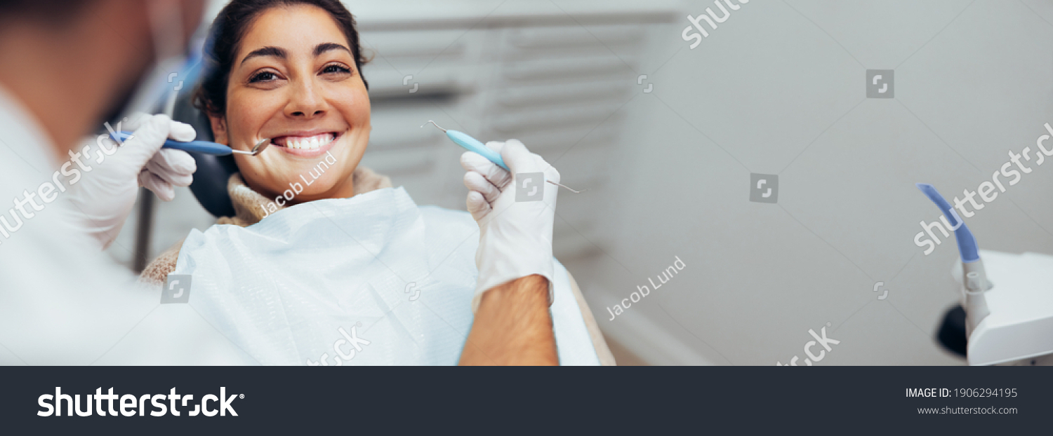 Dentist examining teeth of a female patient in dental clinic using dental tools. Happy woman getting dental treatment. #1906294195