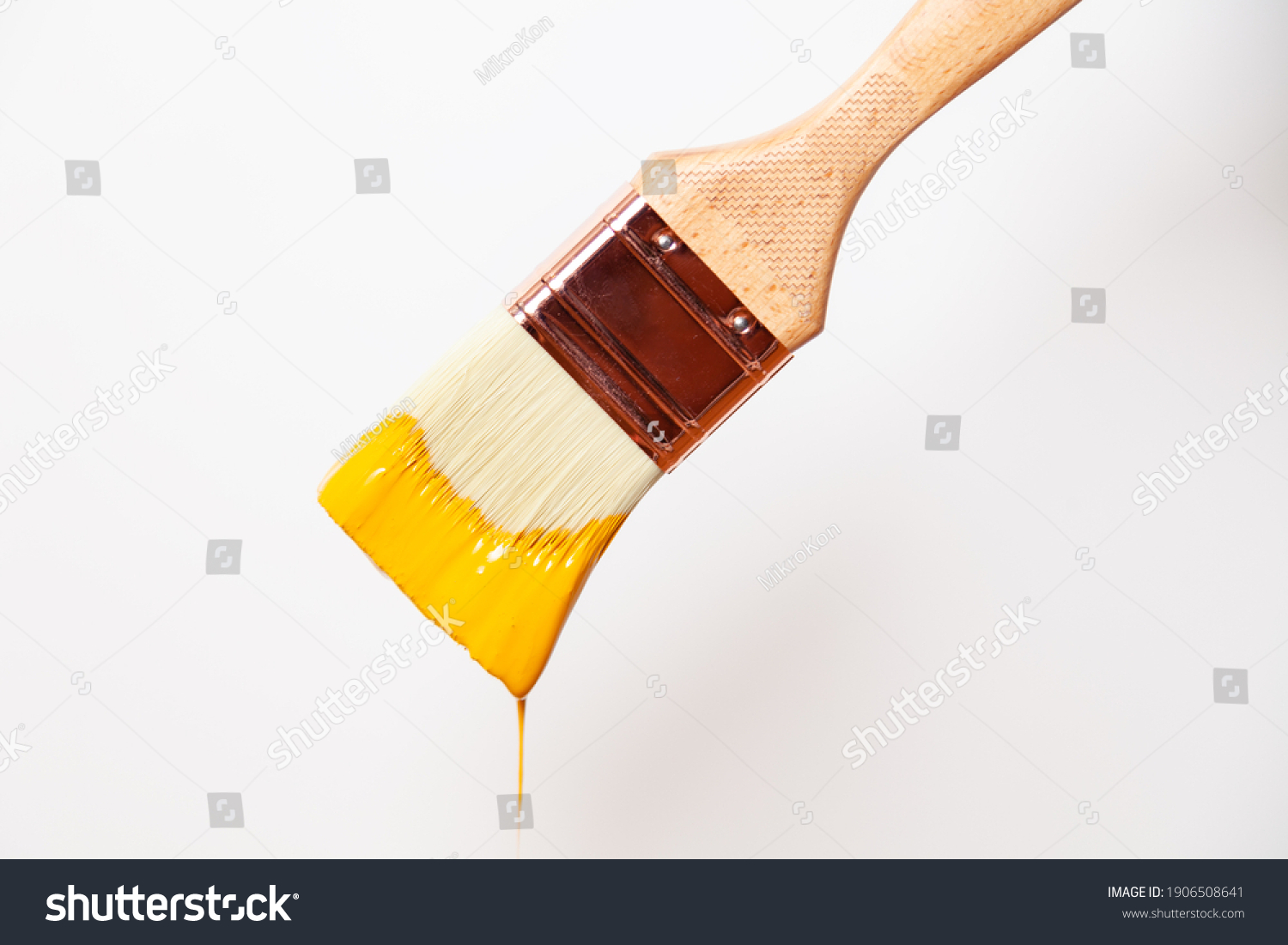 Close-up paintbrush with liquid yellow paint drips off the brush #1906508641