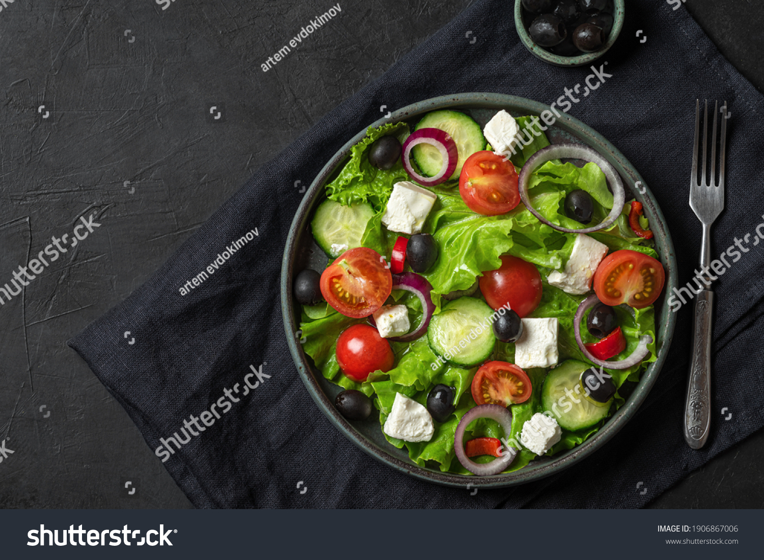 Fresh greek salad with olives, feta cheese, tomato, cucumber, onion with fork on towel on black background. top view. vegetarian food #1906867006