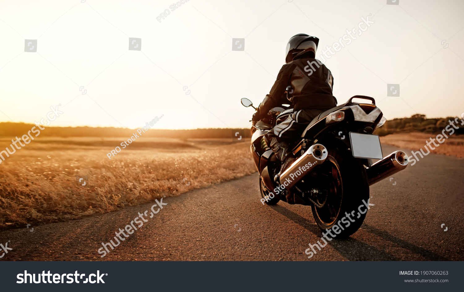 Handsome motorcyclist in leather jacket and helmet at sunset on the road in warm sun rays #1907060263