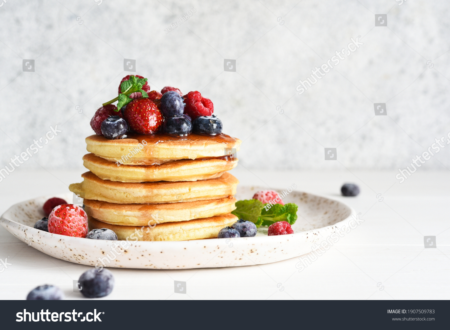 Pancakes with berries and maple syrup for breakfast on a light background. #1907509783