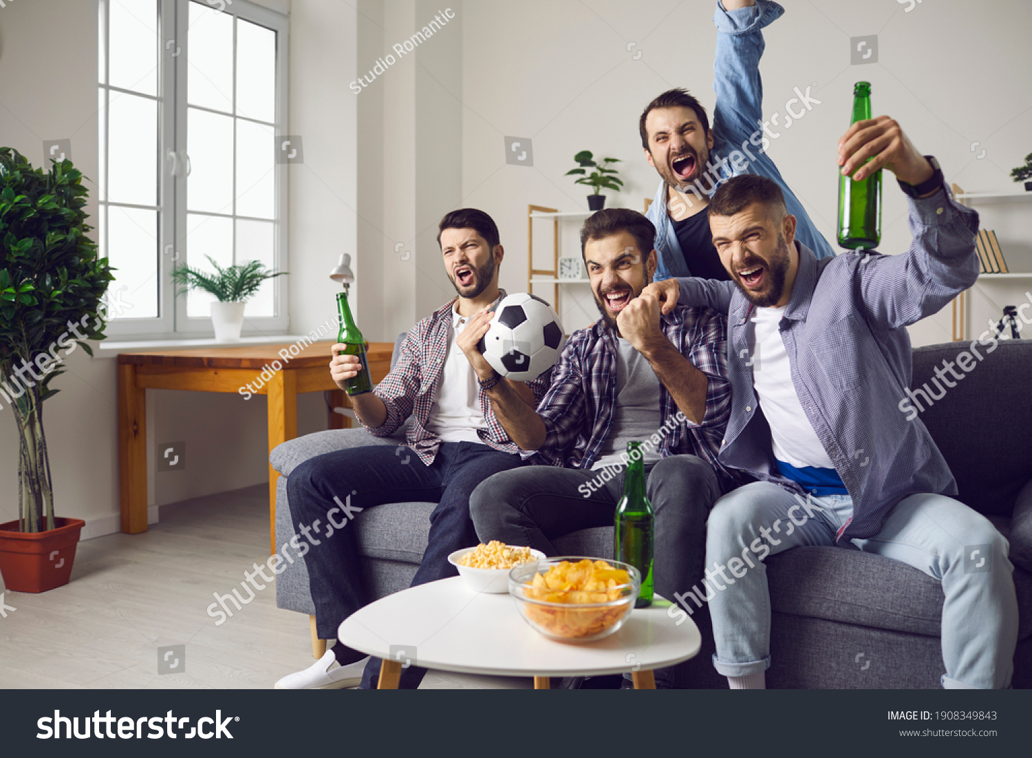 Group of excited men friends football fans feeling happy and celebrating favourite teams goal drinking beer and eating snacks during watching television match at home. Entertainment for male company #1908349843