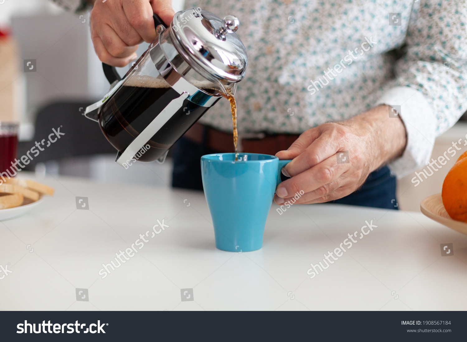 Close up of senior man pouring hot coffee from french press in kitchen during breakfast. Elderly person in the morning enjoying fresh brown cafe espresso cup caffeine from vintage mug, filter relax #1908567184
